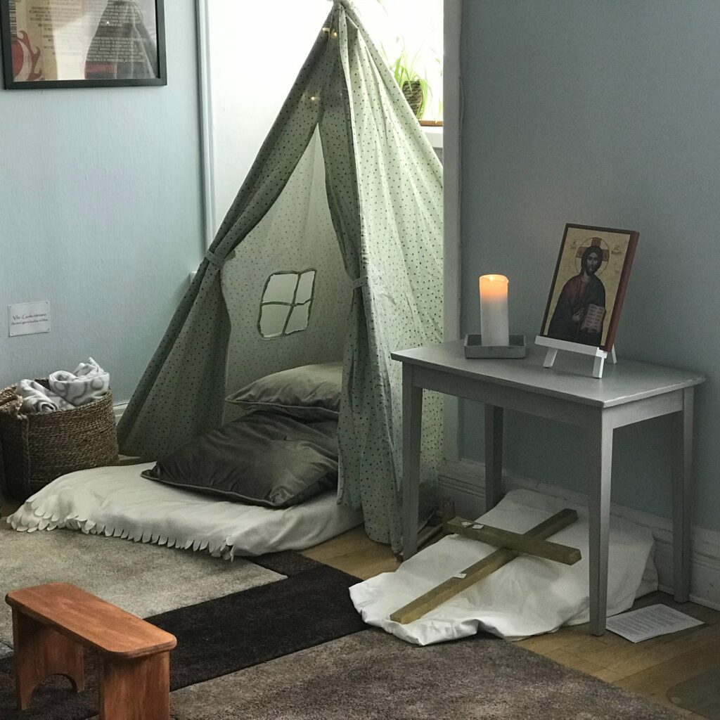 Ett tältliknande kryp-in med kuddar. Ett bord med en tavla av en Jesus-ikon.