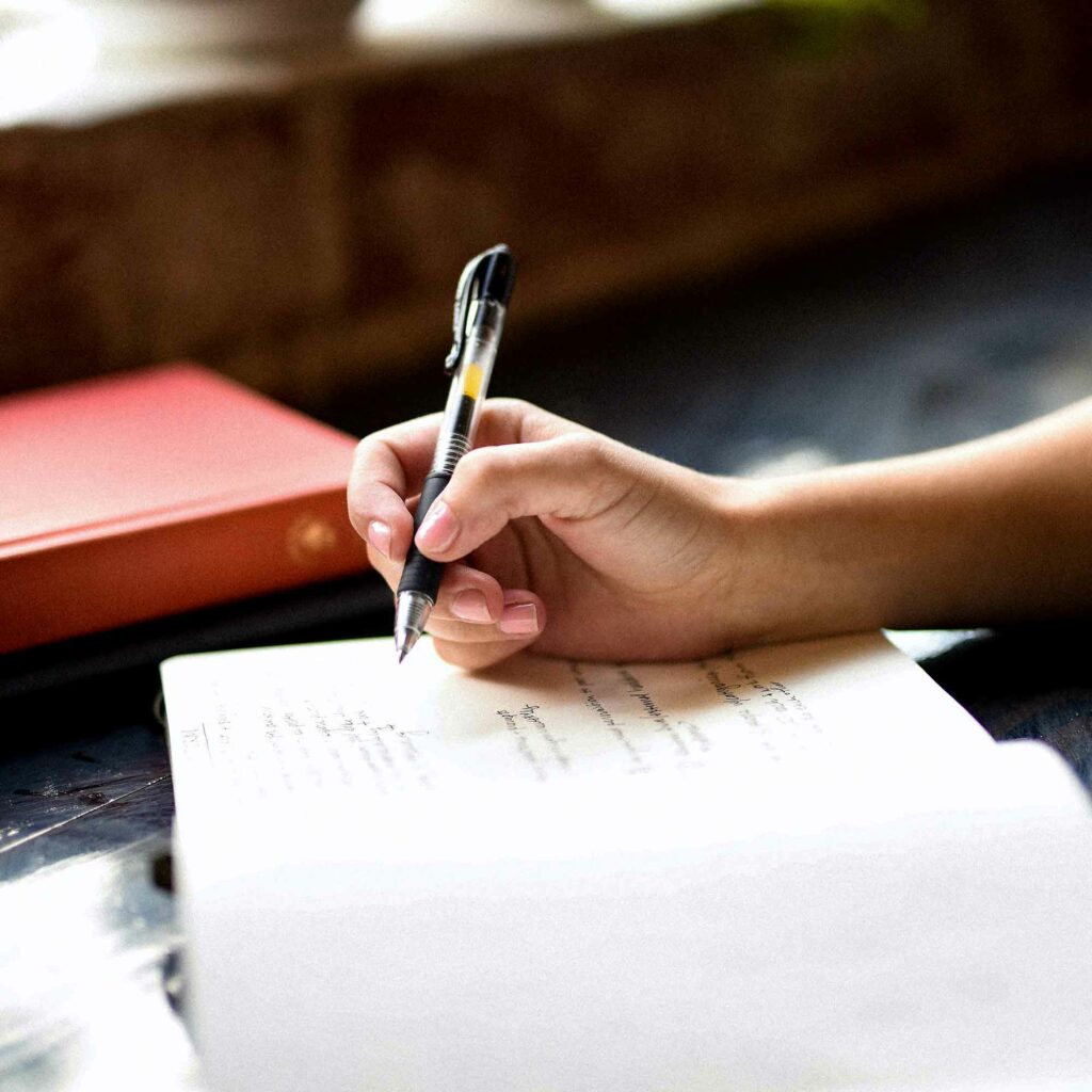 Närbild av en hand som håller en penna över en anteckningsbok
